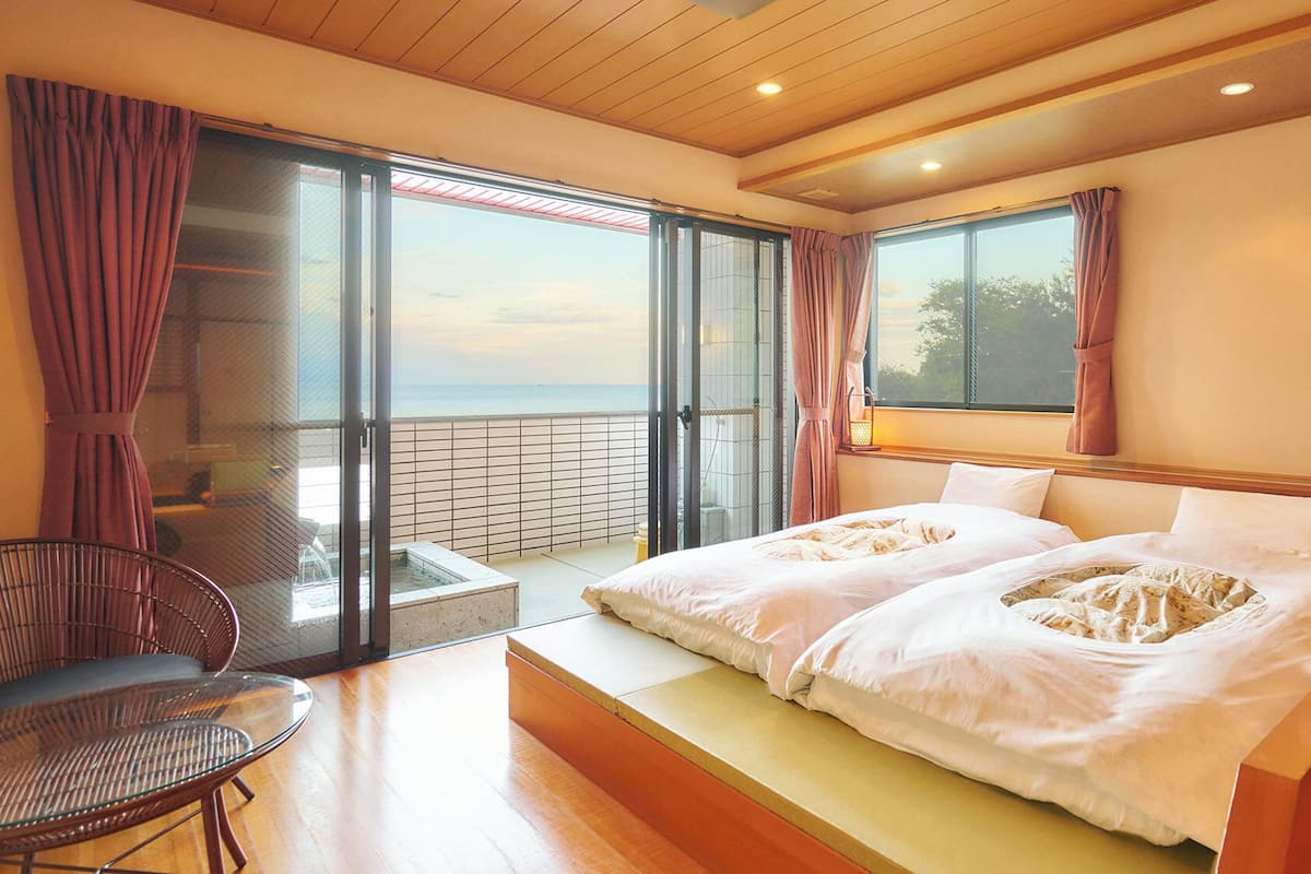 Ein Schlafzimmer mit einem großen Bett, einem Sessel, einem kleinen Tisch und einem Balkon mit Blick.