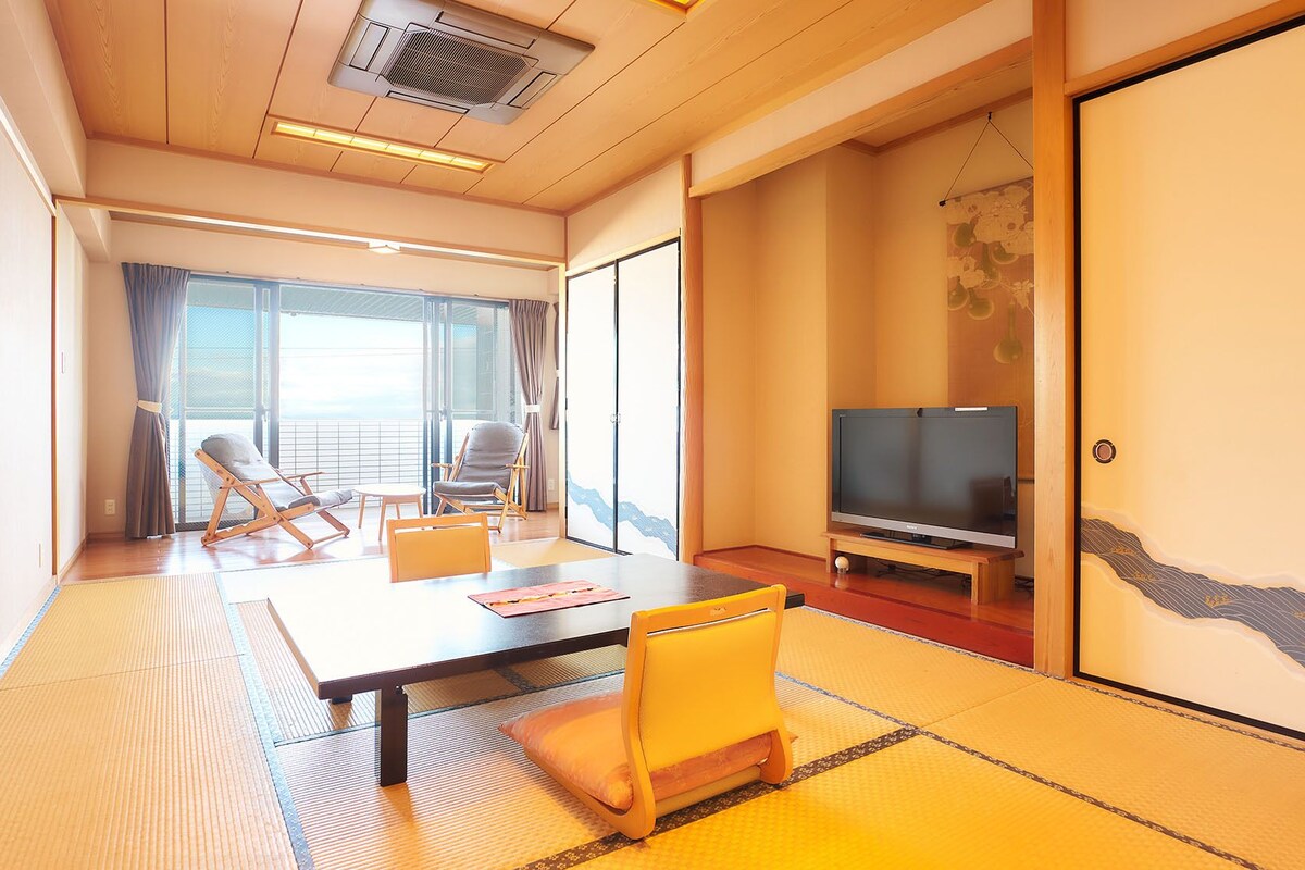 Een hotelkamer met een groot glazen schuifdeur, een flatscreen televisie, een tatami vloer en een traditionele Japanse glijdeur.