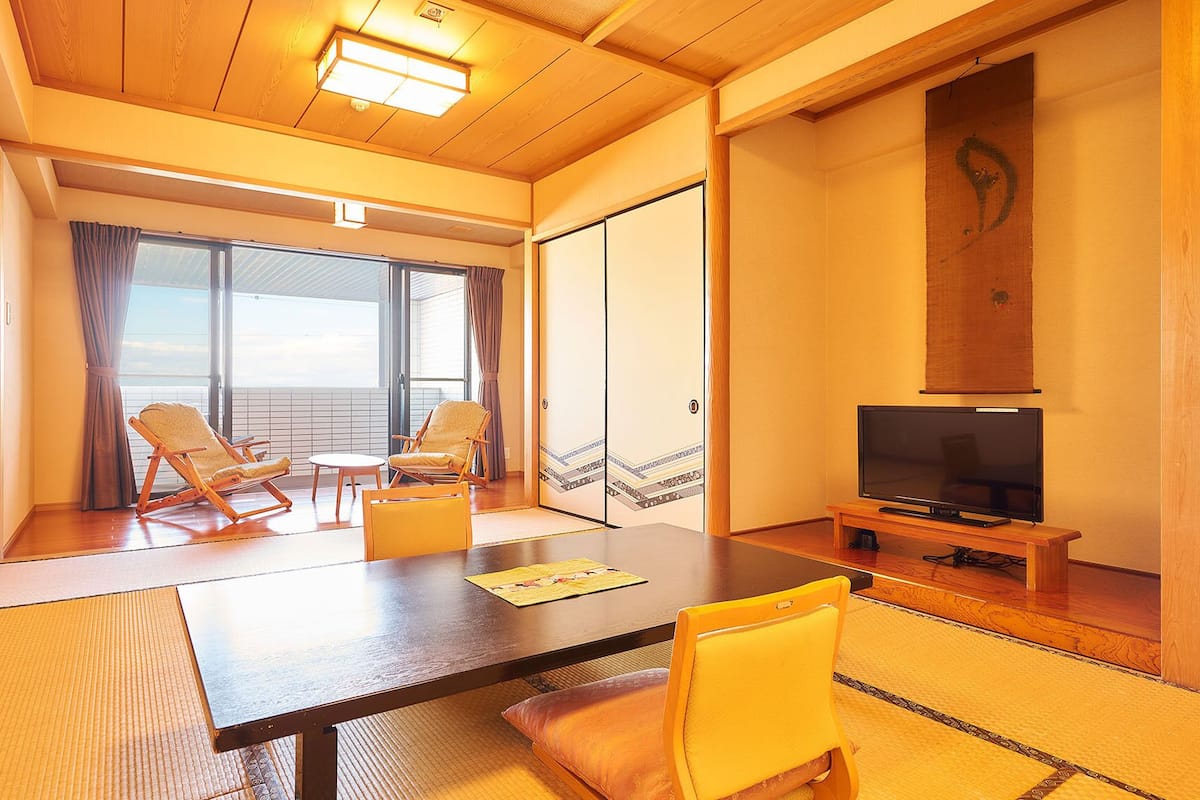 Ein Zimmer mit Holzboden, Tatami-Matte, Fernseher und zwei Stühlen.