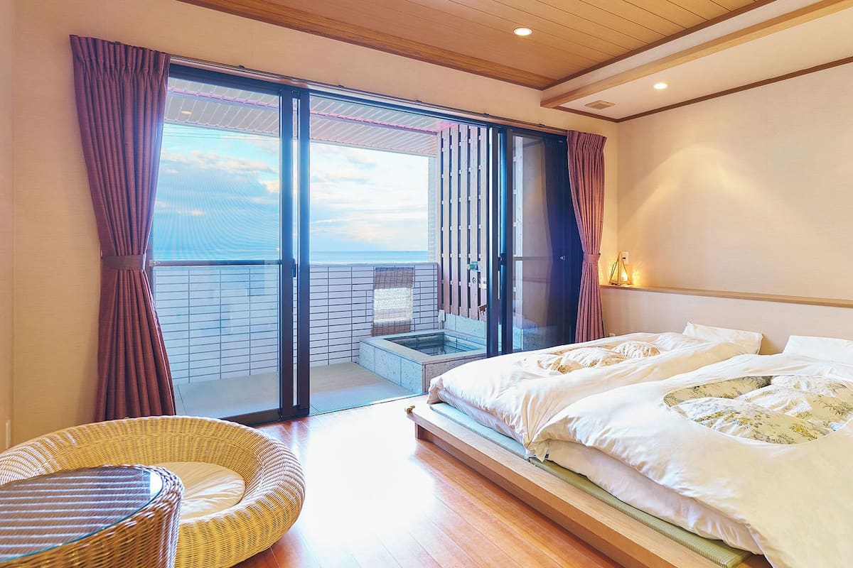 Ein Hotelzimmer mit einem großen Bett, einem Balkon mit Blick und einem Korbsessel.