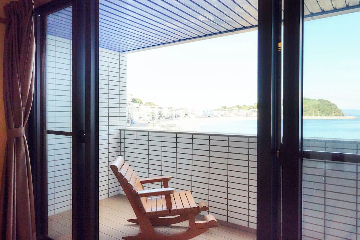 Ein Balkon mit einem hölzernen Schaukelstuhl, Blick auf das Meer und einer gefliesten Wand.