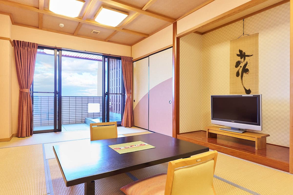 Ein Zimmer mit einem großen Tisch, zwei Stühlen, einem Fernseher und einer Schiebetür zum Balkon.