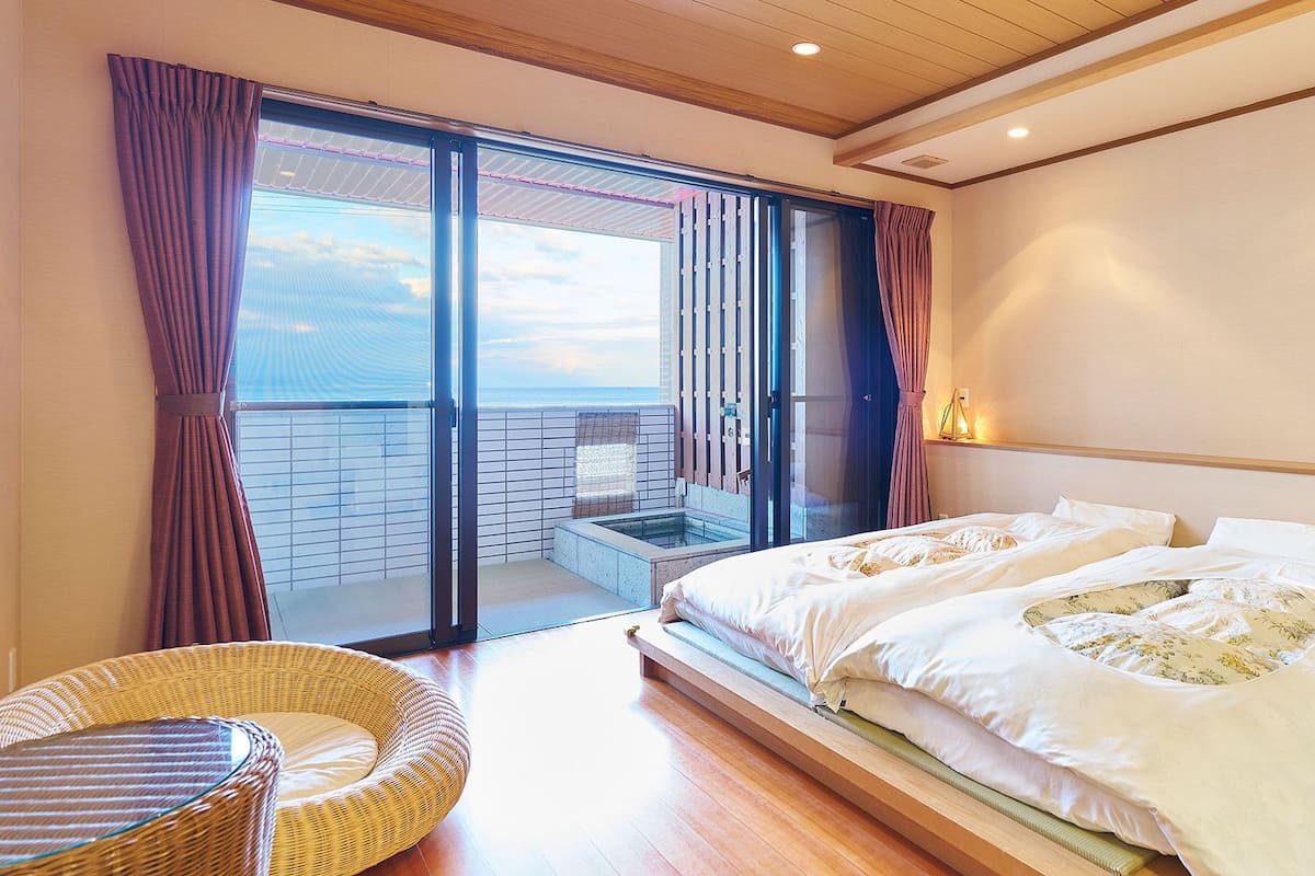Ein Schlafzimmer mit einem großen Bett, einem Balkon mit Aussicht und einem Korbsessel.