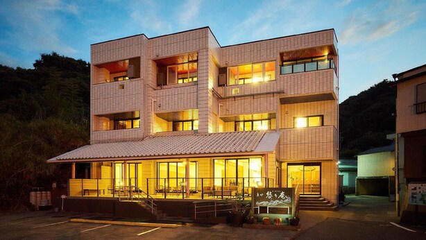 A modern multi-story building with large windows, a covered entrance, and outdoor seating. - Masago Yuyuan (Minamichita)