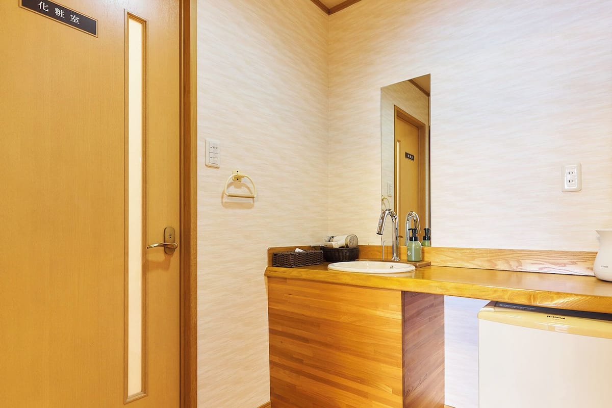 Ein Badezimmer mit einem Holzkosmetikschrank, einem Waschbecken, einem Spiegel, einem Handtuchhalter, einem Wasserkocher und einem Kühlschrank.