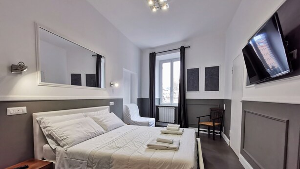 Ett modernt hotellrum med en stor säng, en stol, en TV och ett fönster med gardiner.