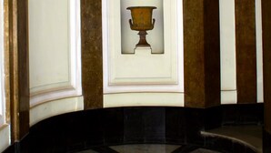 En storslagen hall med en central, välvd alkov, omgiven av höga kolonner, och ett marmorgolv med geometriska mönster.