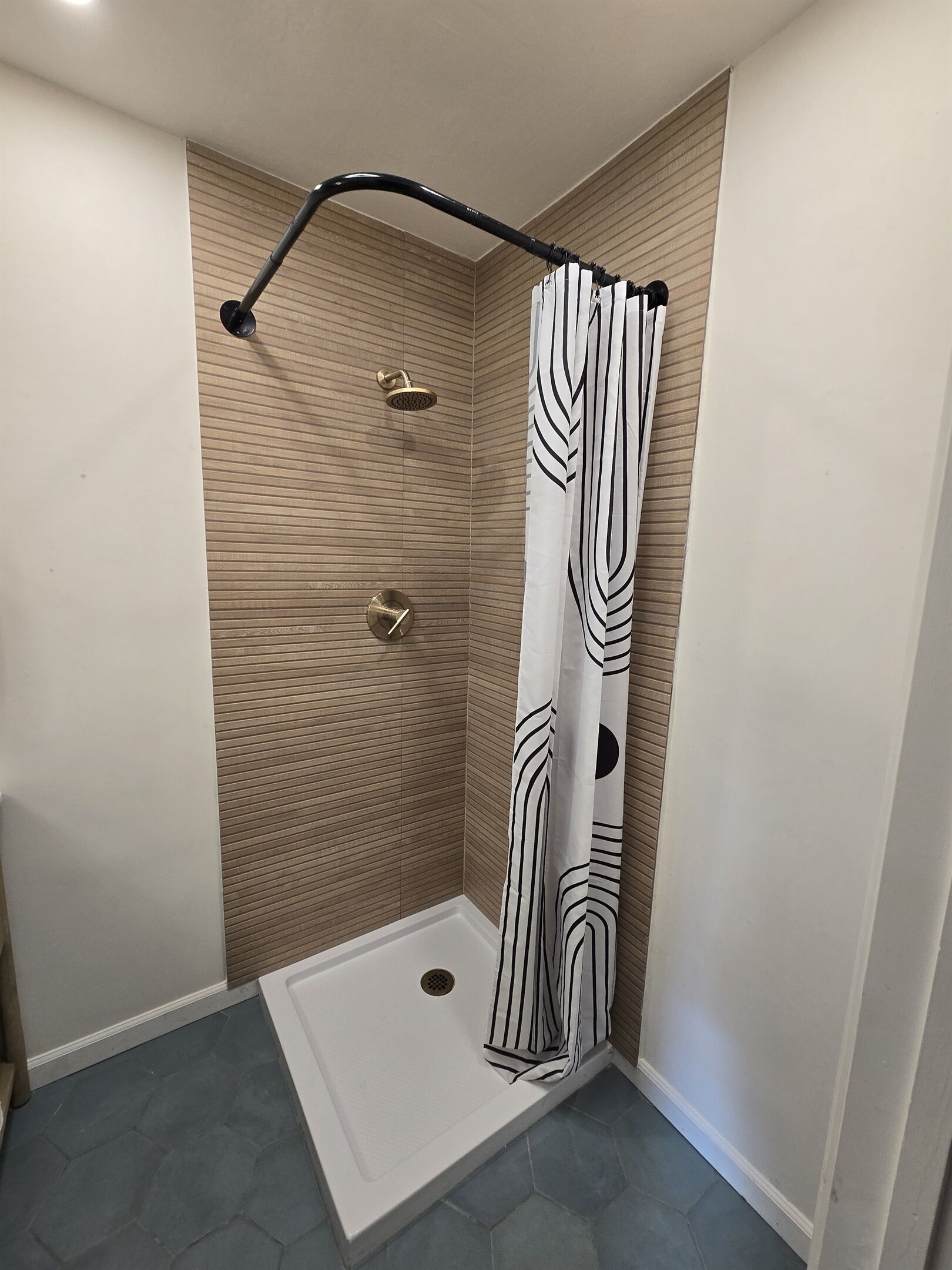 A shower with a curved black hose, a white showerhead, and a patterned shower curtain.