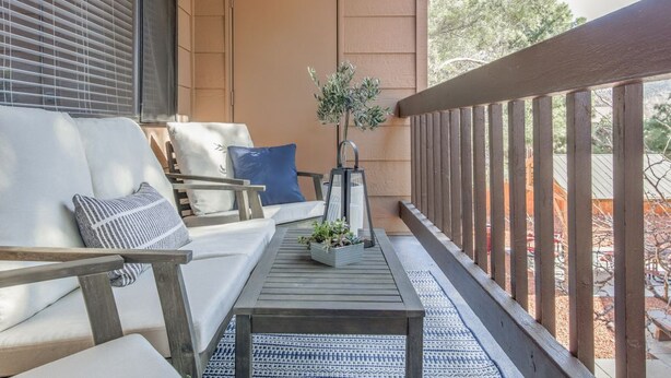 A covered outdoor seating area with a sofa, chairs, a table, and a railing. - Stylish Sedona Condo | Red Rock Views, Modern Comfort & Quiet Location (Sedona)
