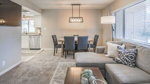 A modern living room with a sofa, coffee table, and dining area with chairs and a table. - Stylish Sedona Condo | Red Rock Views, Modern Comfort & Quiet Location (Sedona)