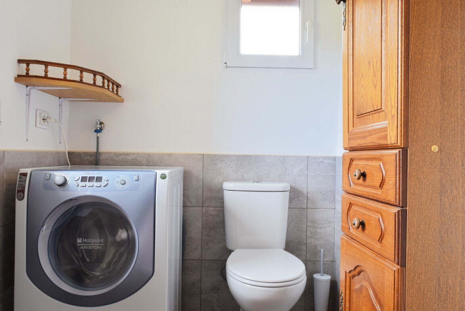 A compact bathroom with a washing machine, toilet, and wooden cabinets.