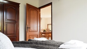 Un dormitorio con una cama grande, un armario de madera y un comedor visible a través de una puerta abierta.
