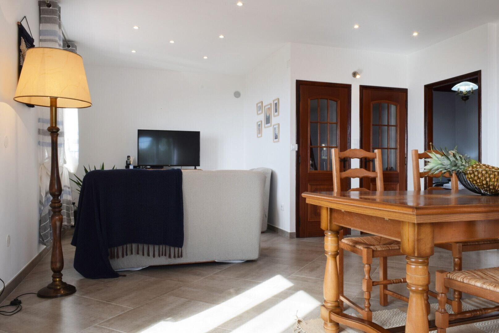 Een woonkamer met een bank, een televisie, een houten eettafel en een lamp.