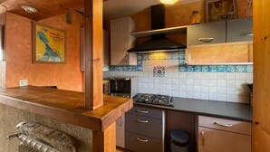 A compact kitchen with wooden cabinets, a gas stove, a microwave, and a tiled backsplash.