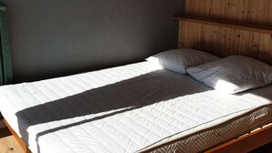 A single bed with a quilted white mattress and two pillows, a wooden headboard, and a wall-mounted lamp.
