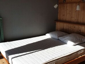 En säng med en personlig sängmadrass och två kuddar, ett huvudgavel av trä och en vägglampa.
