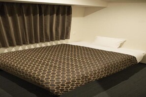 Une chambre d’hôtel avec une couvre-lit à motifs, une grande fenêtre avec des rideaux et un sol recouvert de moquette.