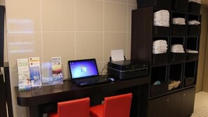 Een receptiebalie met een laptop, brochures en een printer. Er staan rode stoelen en een plank met opgevouwen handdoeken.