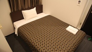 Une chambre d’hôtel avec un lit, une tête de lit, un oreiller blanc, une couvre-lit à motifs et un objet vert sur le sol.