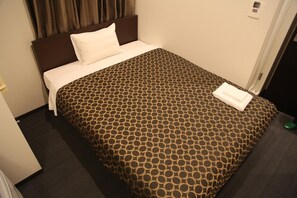 Une chambre d’hôtel avec un lit, une tête de lit, un oreiller blanc, une couvre-lit à motifs et un objet vert sur le sol.