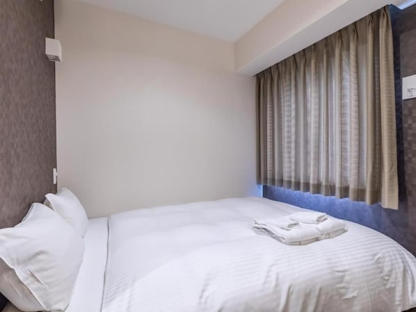 Une chambre d’hôtel avec un lit bien fait, une fenêtre avec des rideaux et un luminaire fixé au mur.