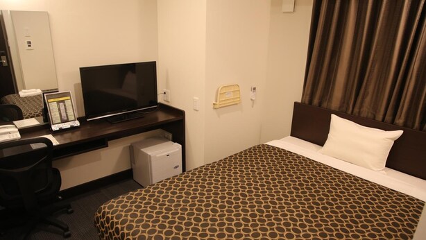 Une chambre d’hôtel équipée d’un lit, d’un bureau avec un ordinateur, d’une télévision et d’un petit réfrigérateur.