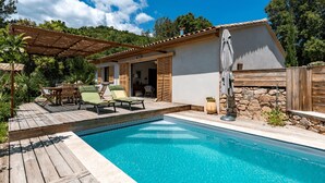 Ein Poolbereich mit Holzterrasse, Liegestühlen und einer überdachten Sitzgelegenheit.
