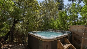 Ein Whirlpool, umgeben von dichter Vegetation, mit einer Holzterrasse und einem Holzbau in der Nähe.