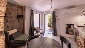 Ein gemütliches Zimmer mit Steingemäuer, einer Couch, einem runden Tisch und einer Küchenzeile.