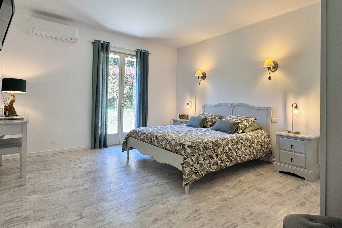 Une chambre à coucher avec un lit, deux tables de chevet, une commode, une lampe et une fenêtre avec des rideaux.