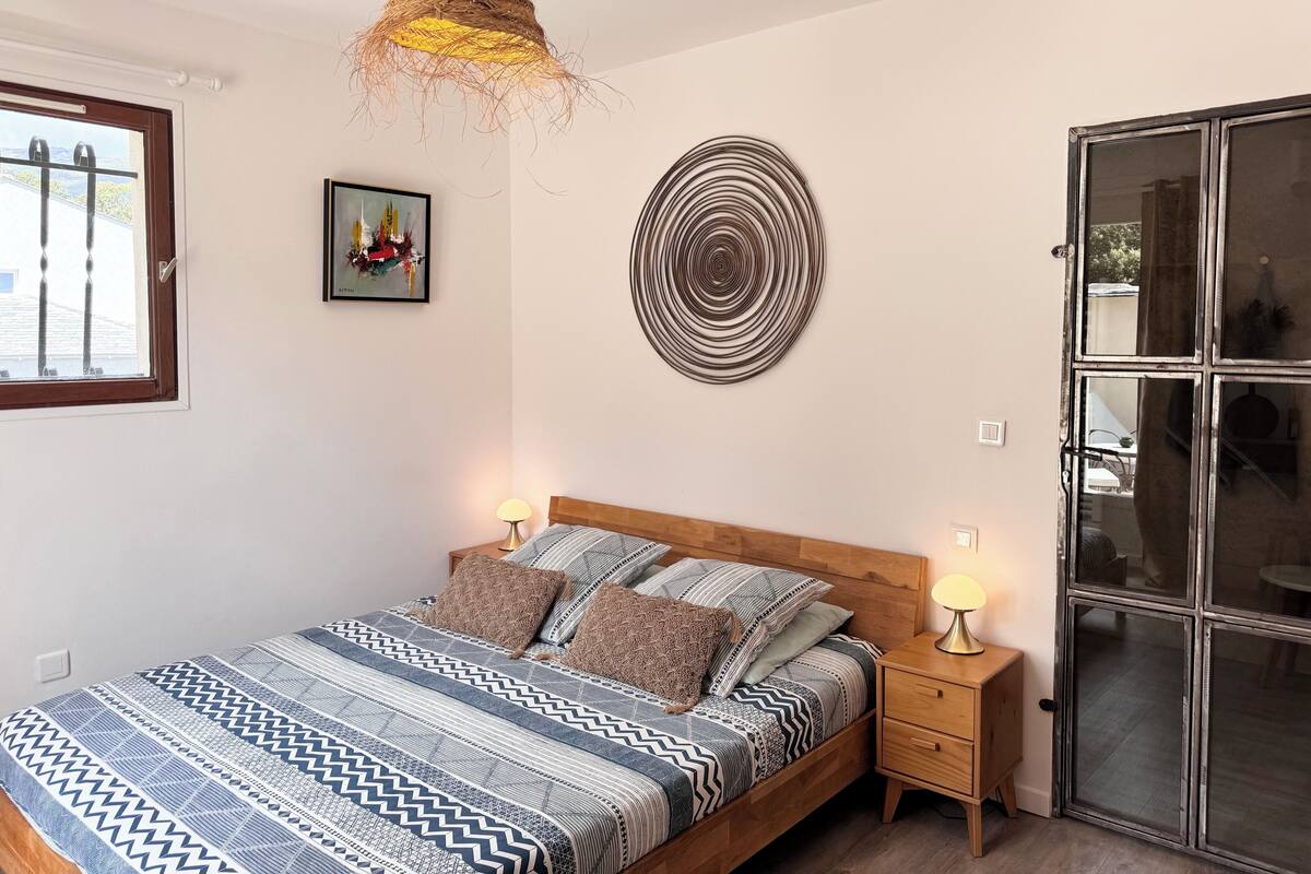 Une chambre à coucher avec un lit, des tables de chevet, un luminaire suspendu et une fenêtre.
