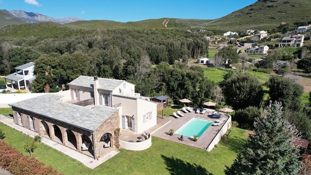 Una villa moderna con piscina, un porche cubierto y vistas de las colinas circundantes.
