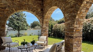 Un porche cubierto con arcos de piedra, mobiliario exterior y vistas a un jardín.
