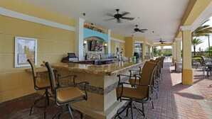 A bar area with a counter, bar stools, ceiling fans, and a tiled floor. - Beautiful Vista Cay Townhome 4006 (Orlando)