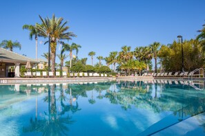 Une piscine d’un bleu éclatant, entourée de palmiers et de chaises longues.