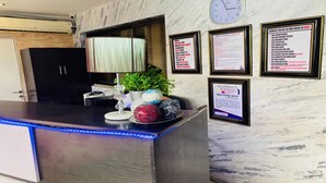 A reception desk with a clock, framed informational posters, and a potted plant. - The Autograph Executive Hotel (Lagos)