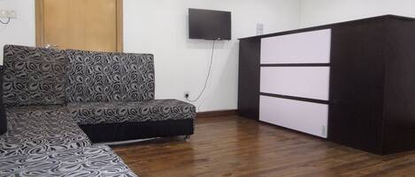 A room with a patterned sofa, a TV mounted on the wall, and a black and white cabinet.