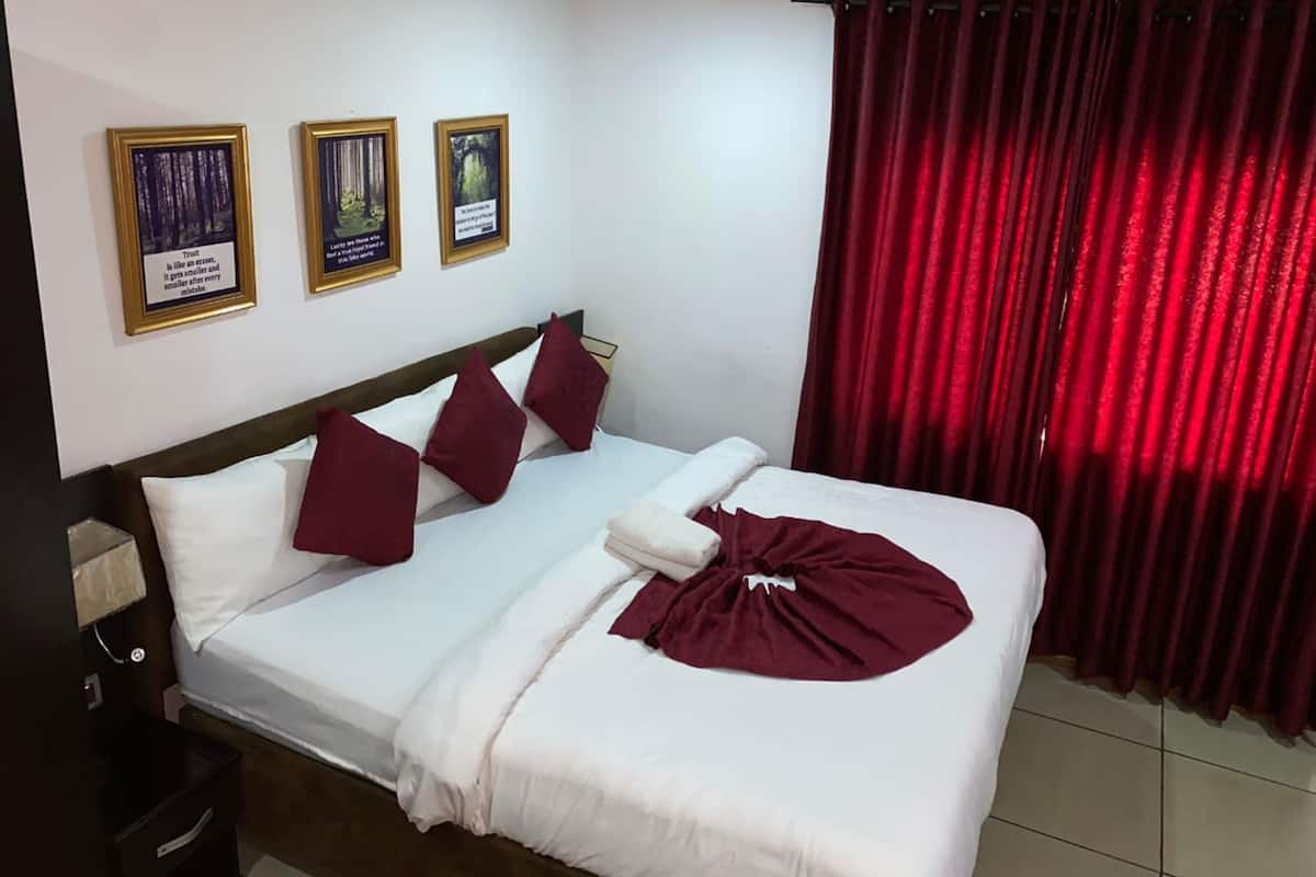 A hotel room with a bed, red curtains, and three framed pictures on the wall.