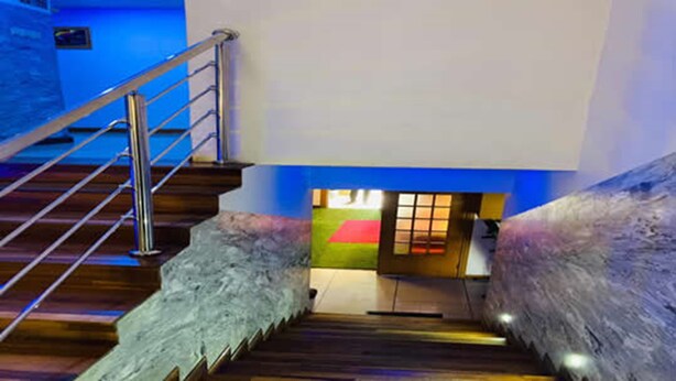 A staircase with metal railings leading to a room with a red carpet and a window with blinds. - The Autograph Executive Hotel (Lagos)