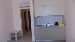 A compact kitchen with a built-in stove, a sink, and a small countertop. There is a bench to the left and a door leading to another room. - Krystal Park studio in Sunny Beach (Sonnenstrand)