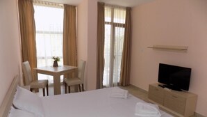 A hotel room with a bed, a TV, a desk with chairs, and curtains. - Krystal Park studio in Sunny Beach (Sonnenstrand)