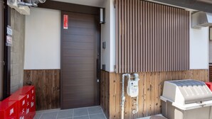 Entrada de un edificio moderno con puerta corredera, cámara de seguridad y una parrilla de barbacoa en el exterior.