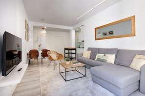 A modern living room with a grey sofa, a coffee table, a TV, and a dining area with chairs and a table.