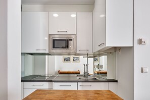 A modern kitchen with white cabinets, a stainless steel microwave, a glass cooktop, and a wooden dining table.