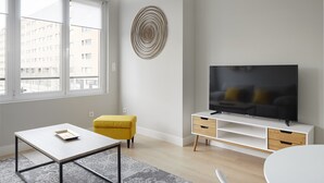 Moderni olohuone, jossa on suuri televisio, keltainen rahi ja pelkistetty sisustus.