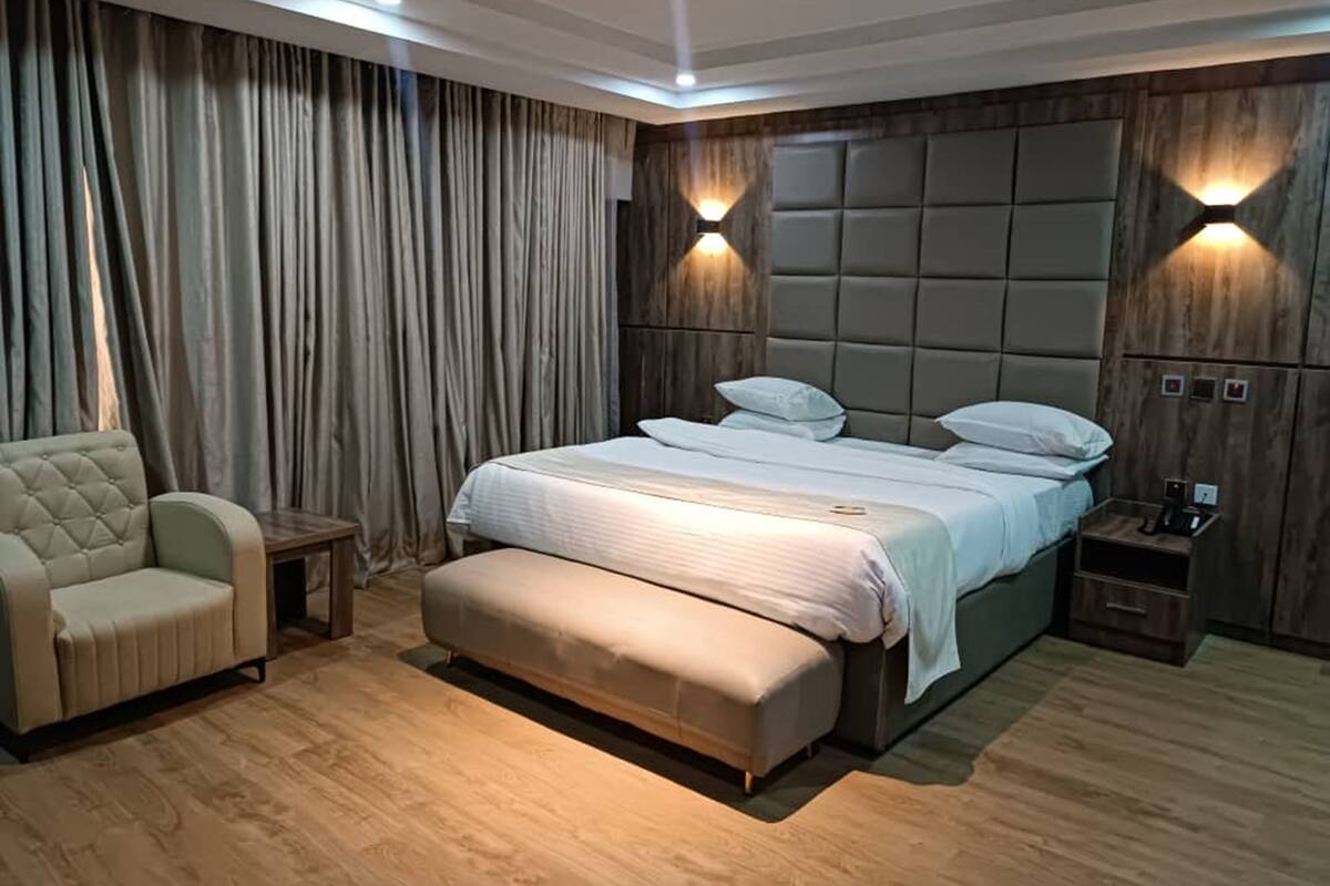A modern bedroom with a large bed, a chaise lounge, and a nightstand with a lamp.