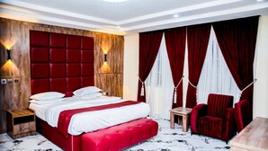Een hotelkamer met een groot bed, een bekleed hoofdeinde in rood, twee bedlampen, een rode fauteuil en een klein houten tafeltje.