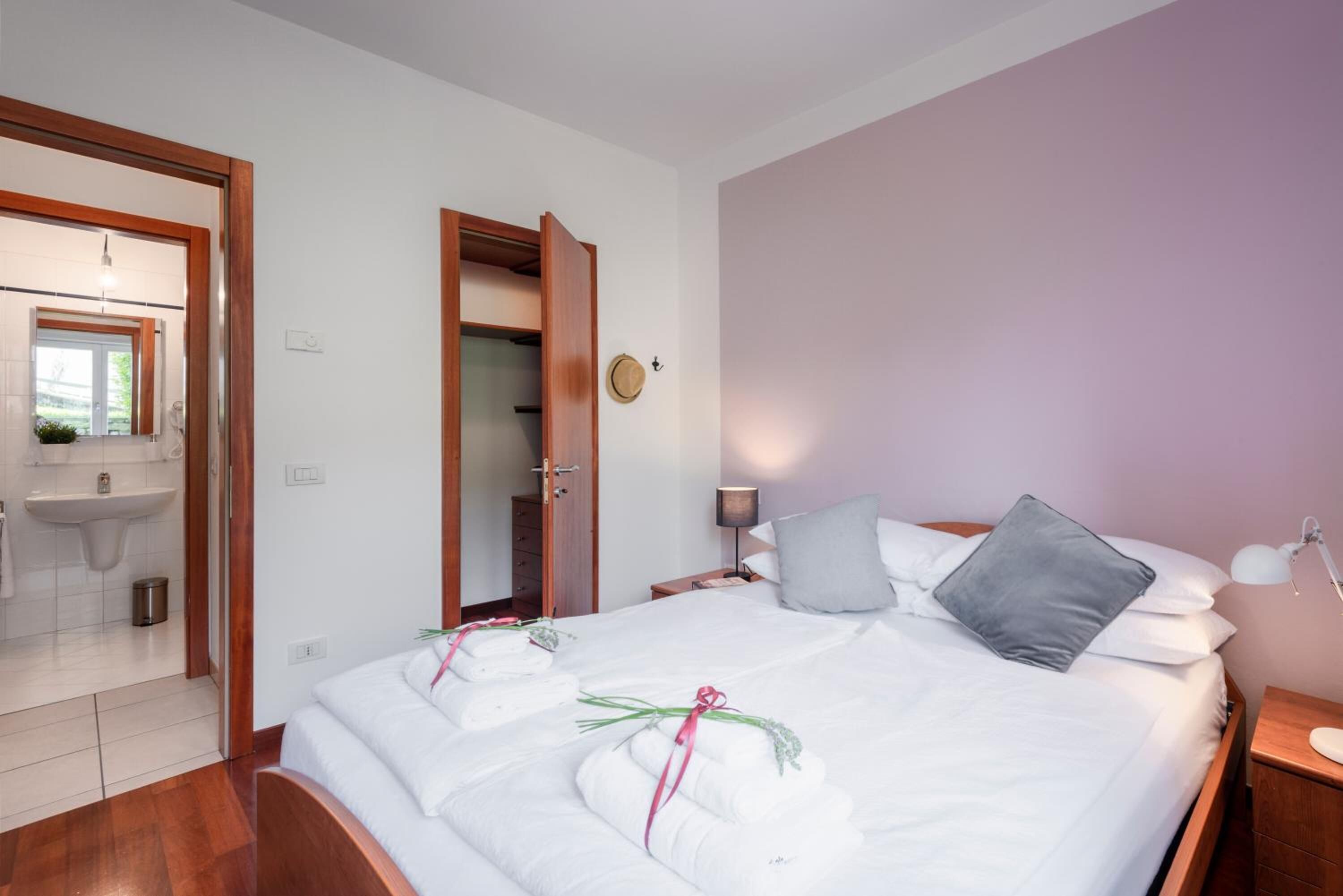 A hotel room with a bed, bedside table, lamp, and a bathroom visible through an open door.