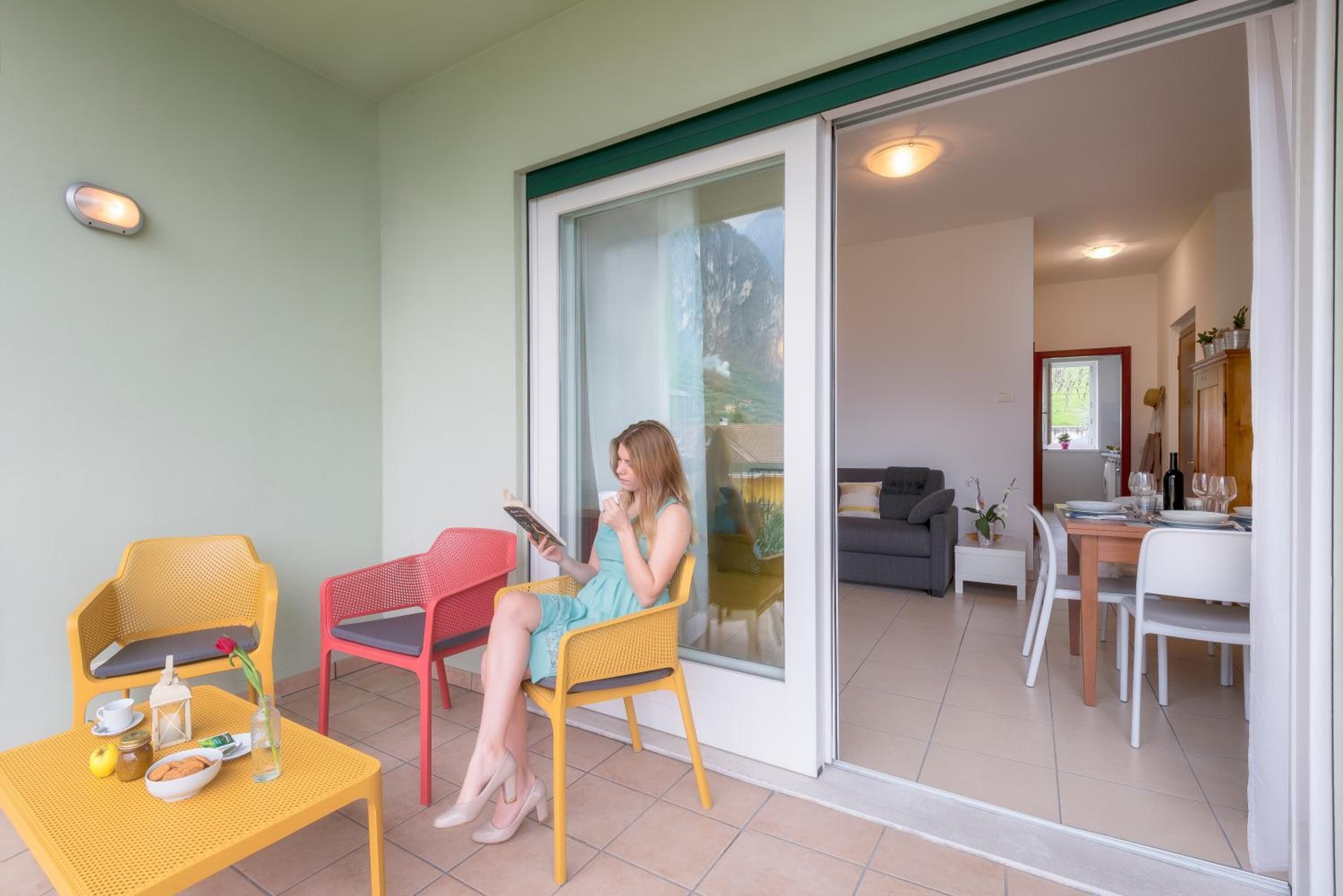 A person sitting on a yellow chair on a balcony with a table and a red chair nearby.