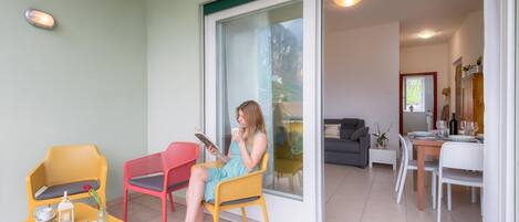 A person sitting on a yellow chair on a balcony with a table and a red chair nearby.